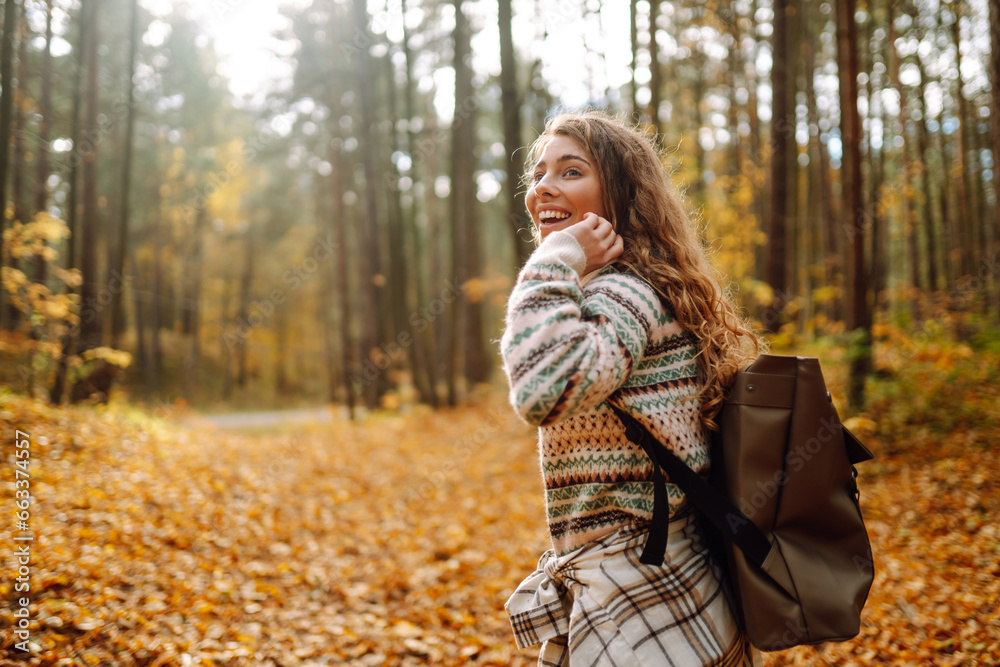 Beautiful young tourist with a backpack is having fun in the autumn forest, throwing fallen leaves. Woman walks along a colorful path in the forest. Freedom, travel. Beautiful young tourist with a backpack is having fun in the autumn forest, throwing fallen leaves. Woman walks along a colorful path in the forest. Freedom, travel.