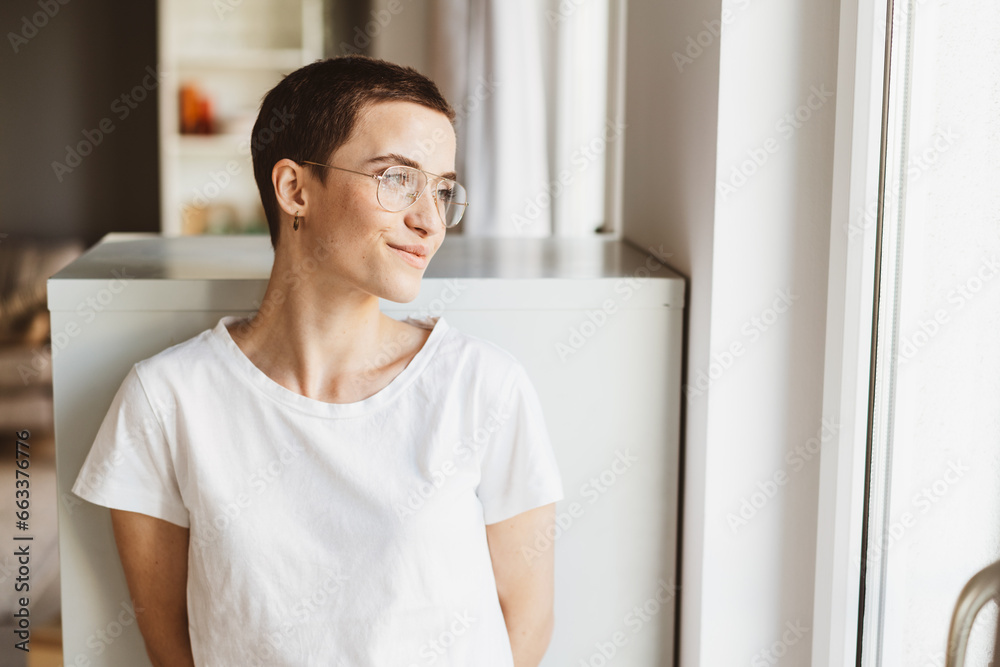 Young Modern Woman with Short Hair and Glasses Contemplatively Smiles out of the Office Window Young Modern Woman with Short Hair and Glasses Contemplatively Smiles out of the Office Window