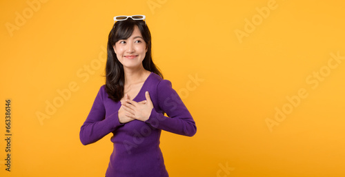 Expressing love and happiness on Valentine's Day, a cheerful young woman forms a heart shape with her hand in a studio portrait, symbolizing romance.