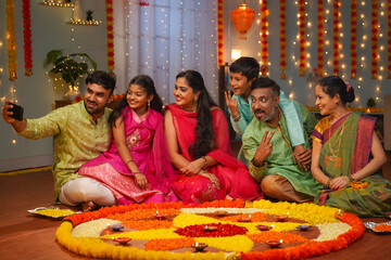 Group of Indian joint family members taking selife in front of decorated diwali rangoli at home - concept of festival gathering, reunion and festival celebration