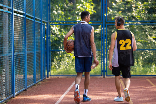 Two men friends players walking on basketball court.