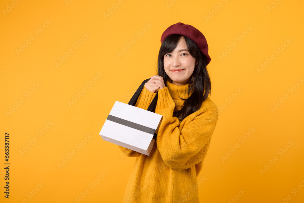 Young Asian woman in her 30s, with a shopping paper bag, showcasing her style in a yellow sweater and red beret against a yellow background. Young Asian woman in her 30s, with a shopping paper bag, showcasing her style in a yellow sweater and red beret against a yellow background.