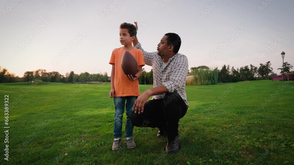 Caring father teaching kid to play rugby on green meadow Caring father teaching kid to play rugby on green meadow