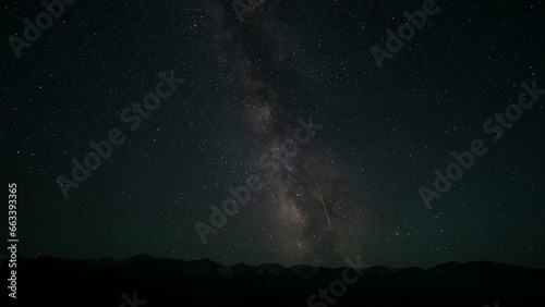 The Milky Way with a falling meteorite on the background of mountains. A bright colored stripe is a trace of a meteorite. Lots of stars. The peaks are covered with snow. Space. Photo for screensaver