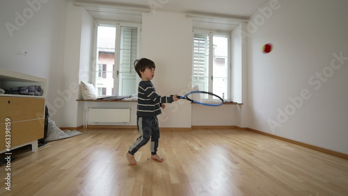 Small boy practicing tennis at home against wall inside empty bedroom. Child hitting ball with racket training coordination