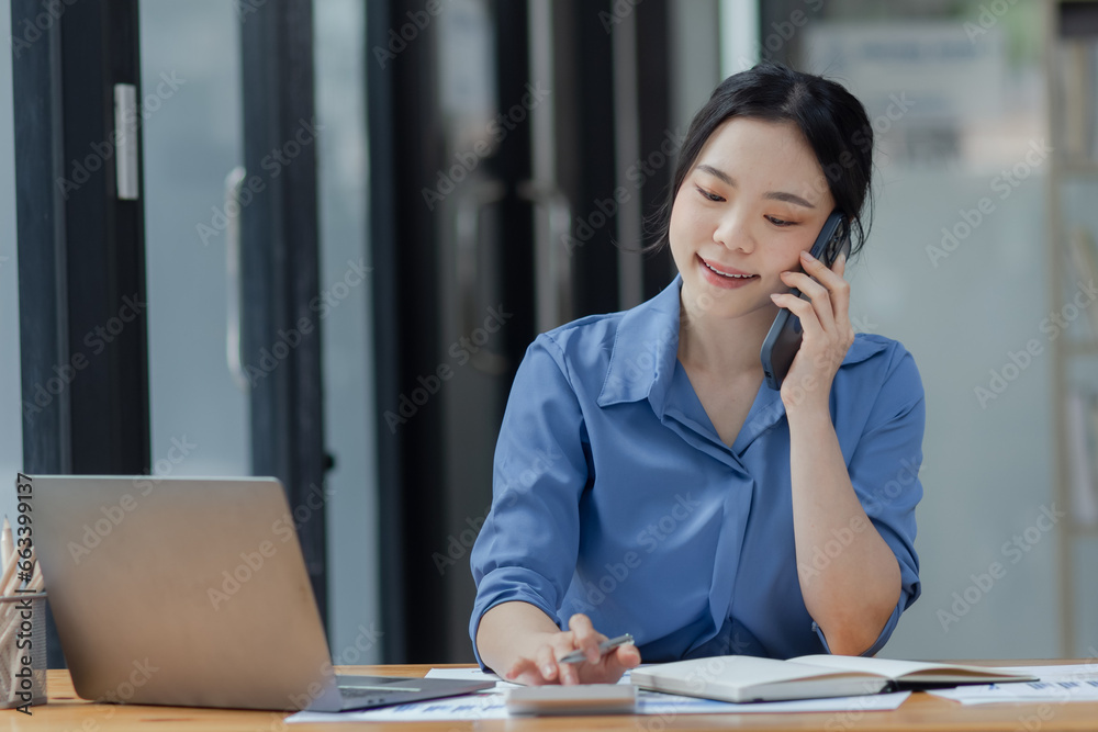Asian businesswoman using smartphone sitting at desk in office, working online, 