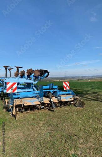 Machinery, equipment for plowing the ground, blue soil stands on green grass against the background of a blue sky. Close-up.