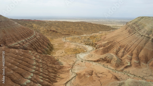 Colorful high mountains and a canyon made of clay. A large gorge with different rocks and different colors. Red, orange, white and yellow flowers of the walls of the rocks. A tourist walks. Aktau photo