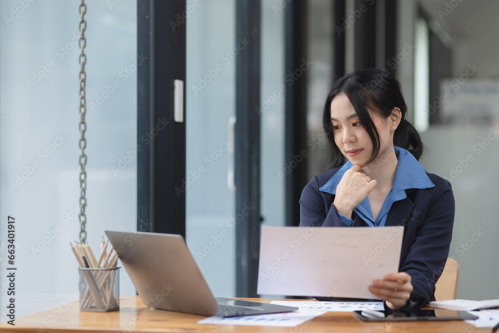 Asian woman working with document papers and laptop sitting at desk workplace office.