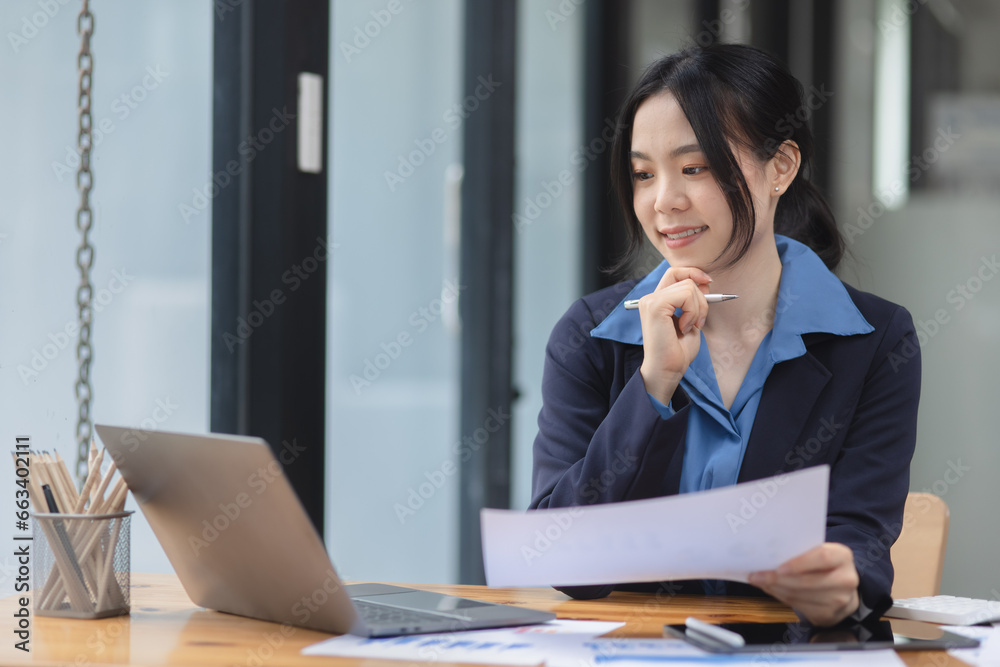 Asian woman working with document papers and laptop sitting at desk workplace office. Asian woman working with document papers and laptop sitting at desk workplace office.