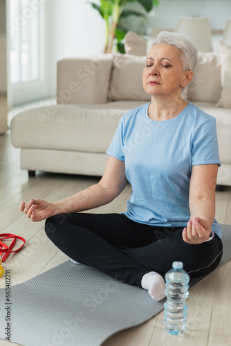 Yoga mindfulness meditation. Senior adult mature woman practicing yoga at home. Mid age old lady sitting in lotus pose on yoga mat meditating relaxing. Older middle aged woman doing breathing practice