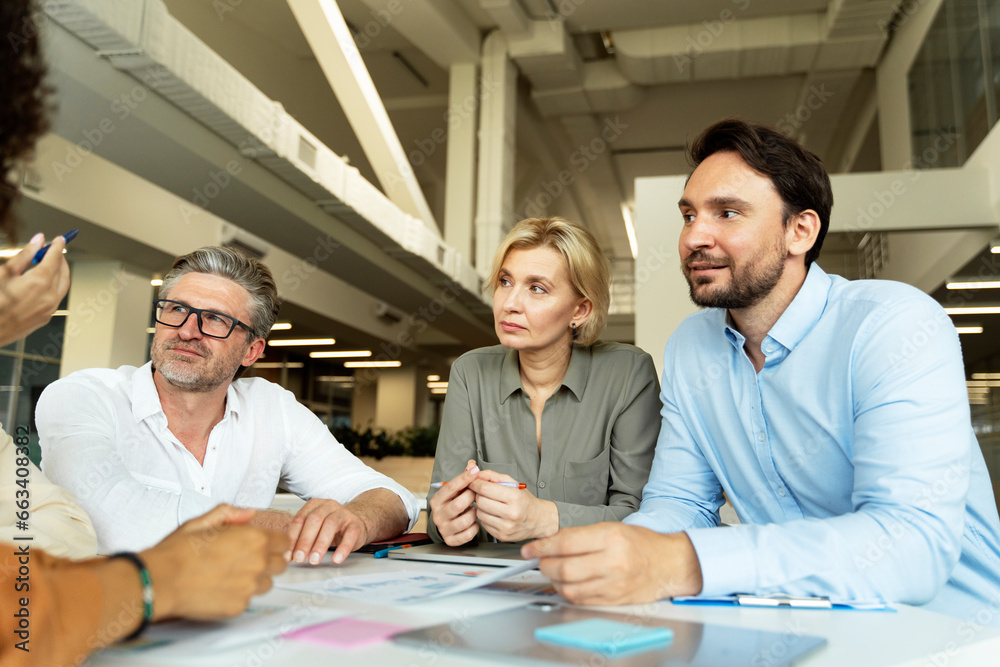Fototapeta premium Middle aged managers sitting at workplace working together, listening to colleague's report