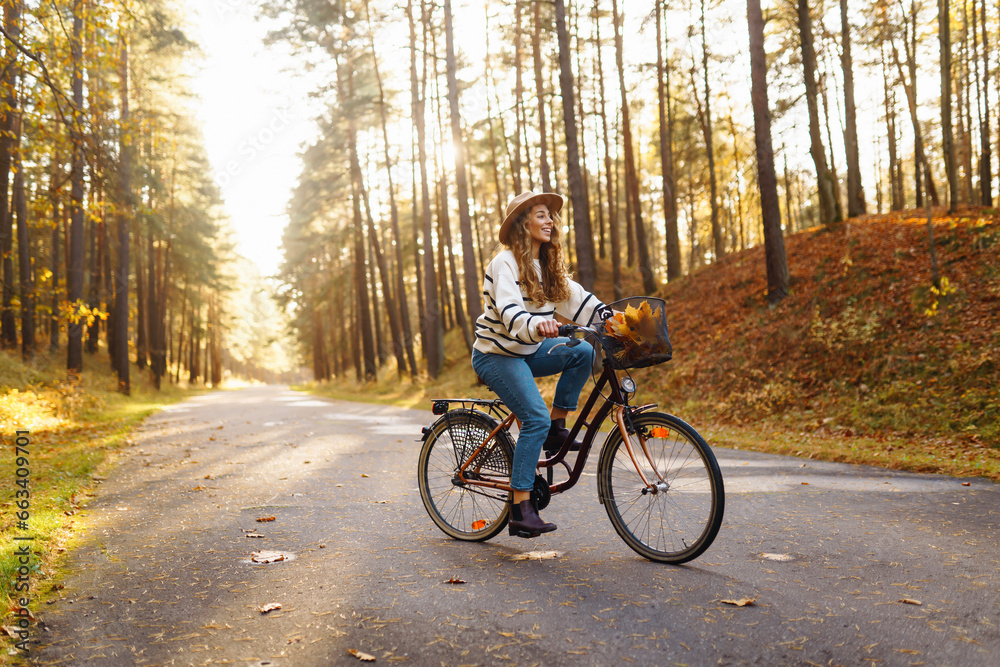 Young woman in a stylish sweater and hat rides a bicycle, feels freedom, enjoys the autumn weather in the forest. Outdoor portrait. Active lifestyle.