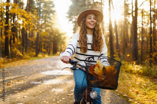 Young woman in a stylish sweater and hat rides a bicycle, feels freedom, enjoys the autumn weather in the forest. Outdoor portrait. Active lifestyle.