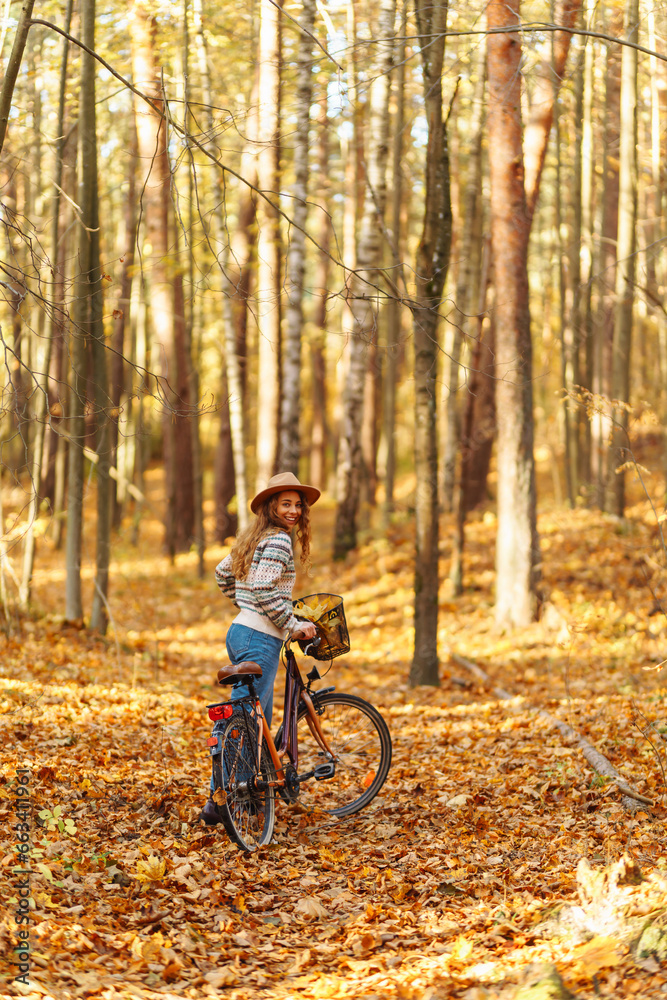 A beautiful woman in a hat and sweater rides a bicycle in an autumn park. Active tourist enjoying sunny weather. Weekend concept. Active lifestyle.