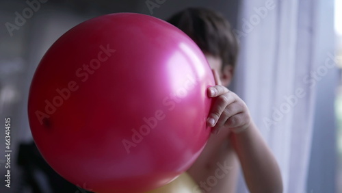 One fun child blowing up balloon with mouth. Happy small boy biting balloon with teeth