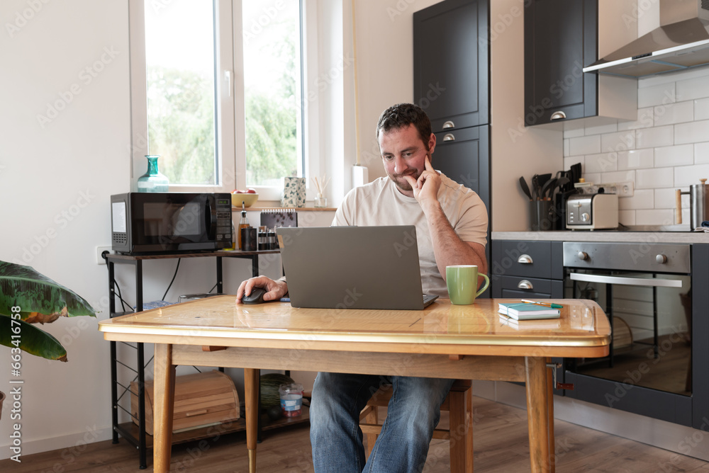 Concentrated man e-learning with his laptop from his kitchen.