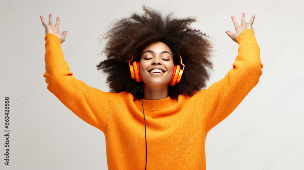Happy young Afro American woman carried away with music dances carefree with arms raised keeps eyes closed wears stereo headphones on ears dressed in orange jumper isolated over white background - obrazy, fototapety, plakaty 
