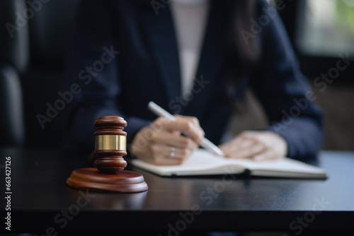 Lawyer woman holding a law book with a wooden legal gavel on an office desk, justice and law concept.