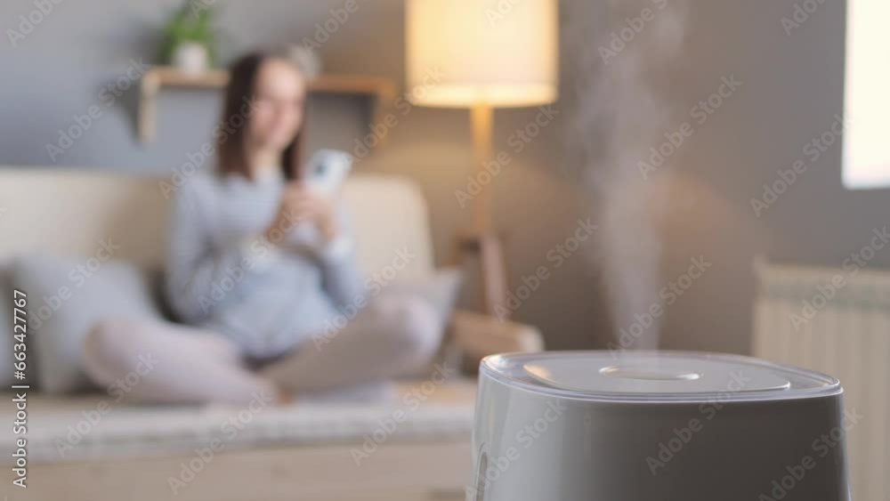 Health microclimate at home. Brown haired woman sitting with air purifier and moisturizer appliance on sofa monitoring air quality in phone.