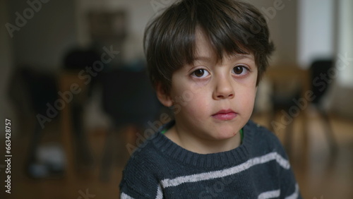 Portrait of a 4 year old boy close-up face looking at camera with neutral expression indoors