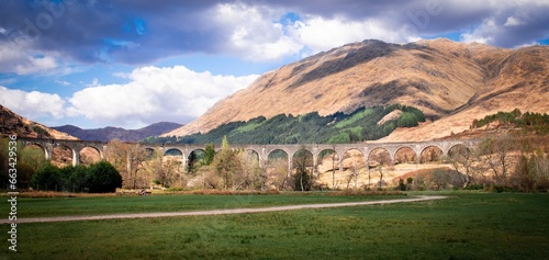 Glenfinnan Viaduct, train bridge, Glenfinnan, Scotland. Famous viaduct in Scottish Highlands, near Fort William, surrounded by hills, blue sky and clouds on a sunny day.