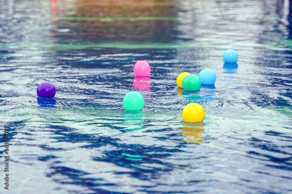 Colorful plastic balls move up and down in the same place on the surface of the water as surface waves, which are transverse waves, pass by.