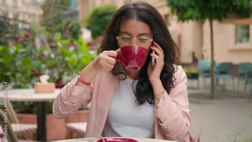 Happy smiling Indian Arabian ethnic woman girl visitor drinking cup coffee in city cafe morning outdoors female businesswoman talking mobile phone business call friendly talk smartphone discuss news Happy smiling Indian Arabian ethnic woman girl visitor drinking cup coffee in city cafe morning outdoors female businesswoman talking mobile phone business call friendly talk smartphone discuss news