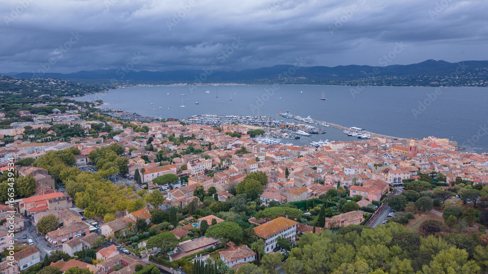 Aerial view of  Saint-Tropez and the marina. Photography was shot from a drone at a higher altitude with the bay in the background, on a cloudy day. Photo was taken from a drone from above the city.