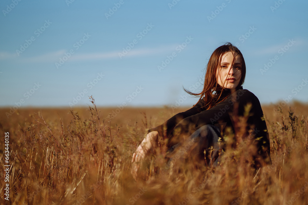 Young woman in a coat standing in a field among dry grass, enjoying nature. Urban style and street fashion. Concept of nature, fashion, freedom. Lifestyle.