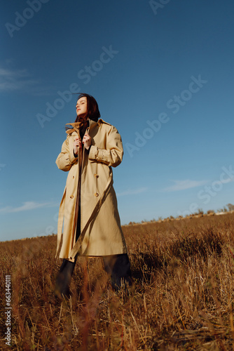 Young woman in a coat standing in a field among dry grass  enjoying nature. Urban style and street fashion. Concept of nature  fashion  freedom. Lifestyle.