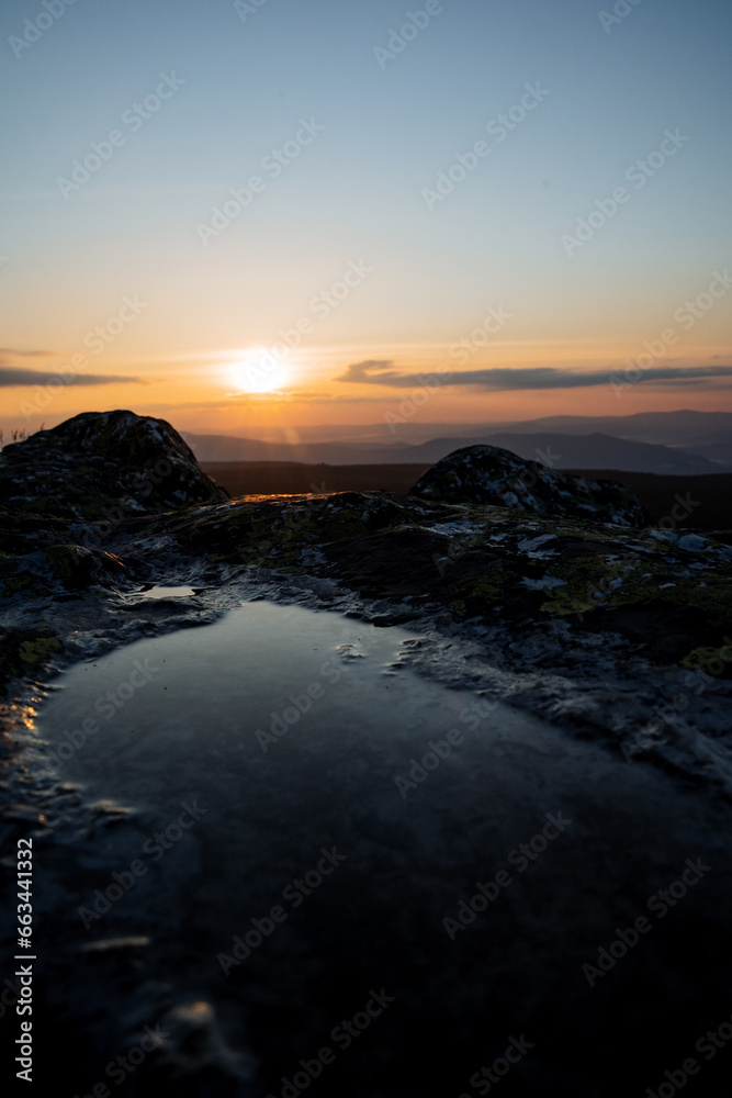 Morning dawn in the mountains, the reflection of the sky in a puddle of water on a stone, water gathered in a rock recess, the sun on the horizon.