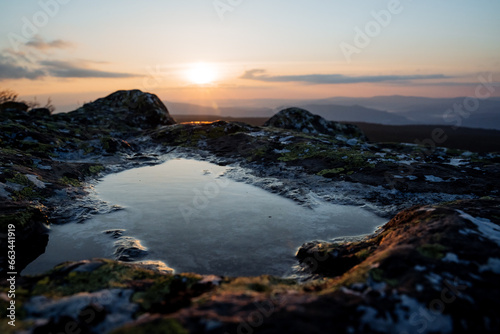 A puddle on a stone from a dew in the mountains, the dawn of the sun in a mountainous area, the reflection of the sky in the water, a stone lake.