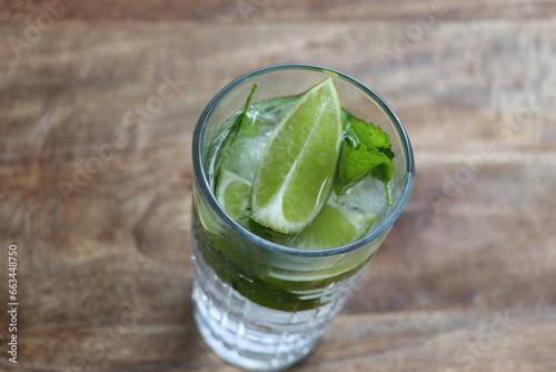 Glass of Mojito summer alcoholic cocktail with ice cubes mint and lime on wooden background