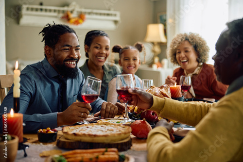 Happy black multigeneration family toasting during Thanksgiving meal at dining table.