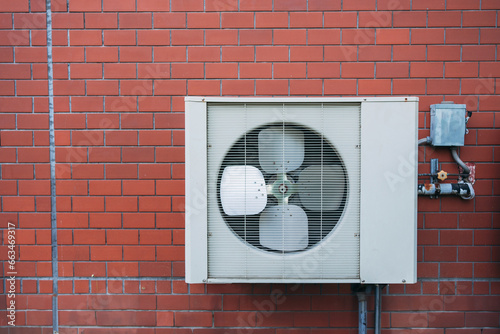 Air conditioner compressor installed on the wall of a building, along with industrial air conditioning units and ventilation systems. Cooling systems.
