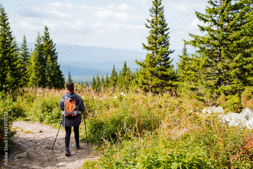 A girl with a backpack walks along a trail in the mountains, a solo journey through the taiga terrain, a road in the forest.