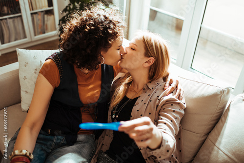 Young lesbian couple sharing a kiss after a positive pregnancy test at home photo
