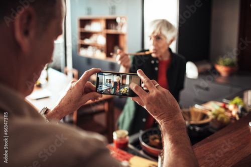 Mature woman doing a taste test for a picture taken by her husband in the kitchen at home photo