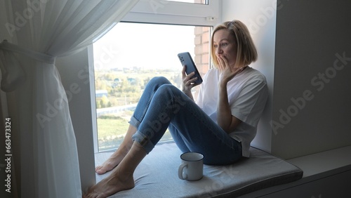 Wallpaper Mural Woman ordering goods online in applications, on the Internet. A young woman uses a mobile phone near the window at home. Torontodigital.ca