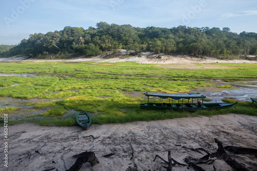 Boat stranded on dry river in extreme drought in the Amazon Rainforest, the largest tropical forest in the world. Concept of climate change, global warming, environment, ecology, disaster, weather.