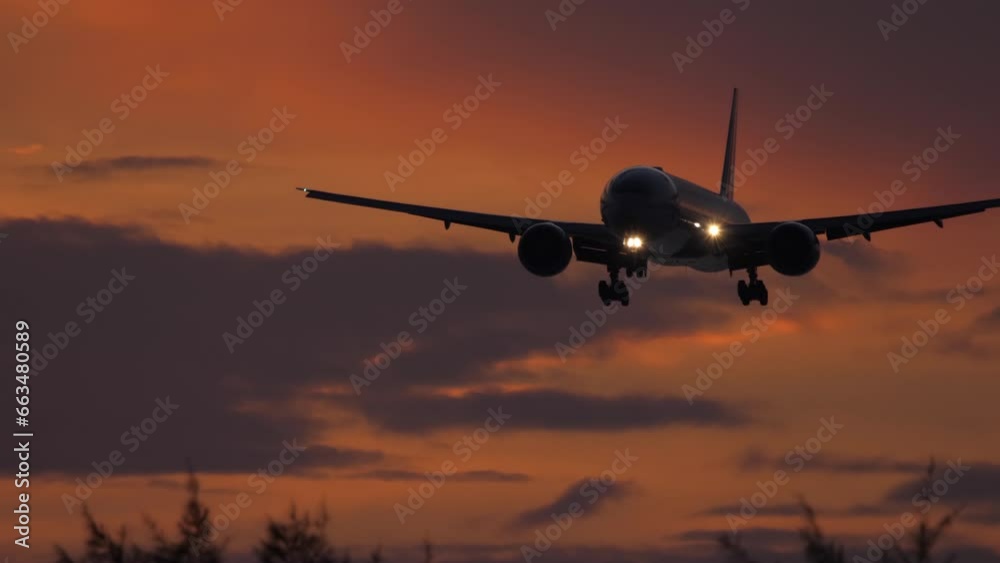 Silhouette of air plane landing at cloudy sunset with beautiful red sky and sun in background Silhouette of air plane landing at cloudy sunset with beautiful red sky and sun in background