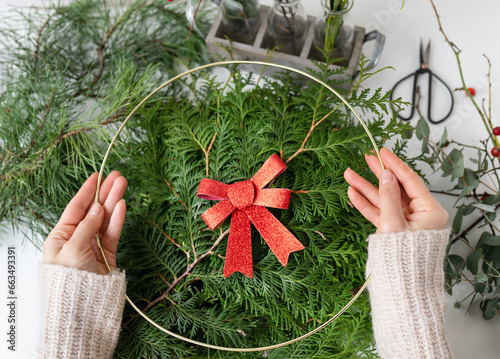 The concept of preparing for Christmas and New Year. A girl makes a Christmas wreath, the process of making a Christmas wreath from pine needles, thuja, shimia, rose hips, pine twigs. photo