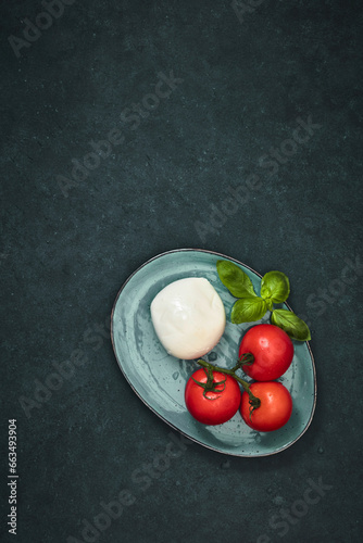 Fresh cherry tomatoes, basil, mozzarella cheese on black slate stone table. Healthy Italian traditional salad ingredients. The concept of organic Mediterranean cuisine, apartment, close-up.
