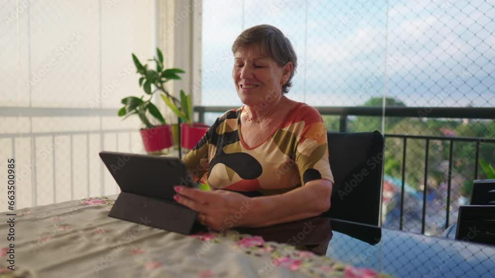 Happy senior woman using tablet at home. Older mature female person looking at modern technology screen at apartment balcony