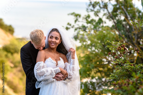 Newlyweds hug against the backdrop of a beautiful landscape, the guy kisses the shoulder of a girl who has a happy look