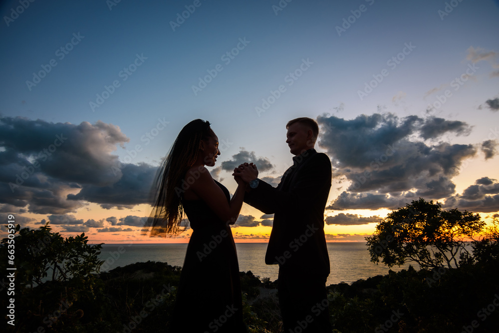 Happy young couple holding each other's hands in backlight against sunset background