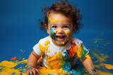 a messy and joyful toddler playing and covered in colorful paint on blue background