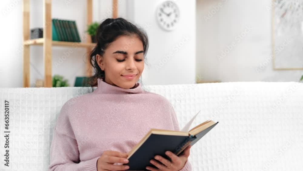 Beautiful brunette young woman reading interesting book sitting on comfortable couch at white room Beautiful brunette young woman reading interesting book sitting on comfortable couch at white room