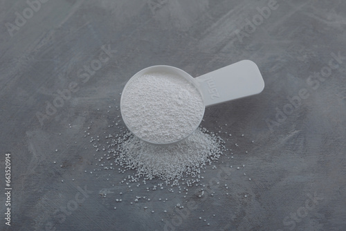 Sodium percarbonate or sodium carbonate peroxide in measuring spoon. White granulated powder. Chemical substance with formula Na2H3CO6 used in eco-friendly bleaches and other cleaning products photo